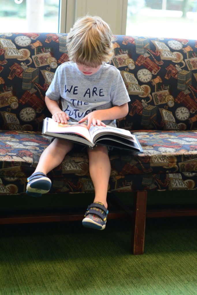 Young boy reading on couch. His shirt says "we are the future."